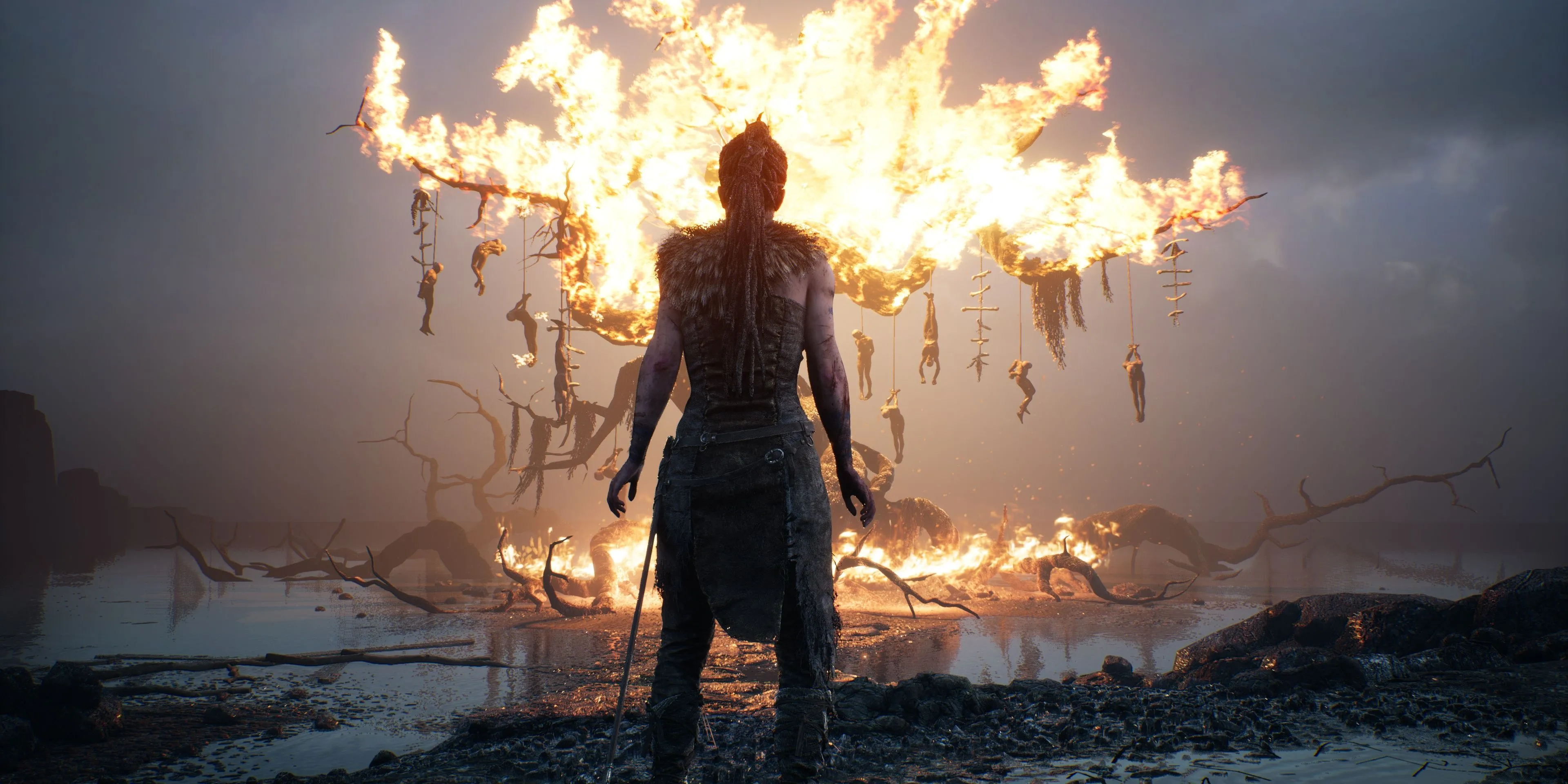 Senua đứng trước một cây đang cháy trong Hellblade: Senua's Sacrifice, ánh sáng đỏ chiếu rọi